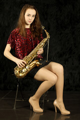 Young girl with saxophone sitting on chair in black room