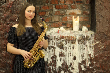 Portrait of young woman with saxophone in front brick wall with candle and wax coating