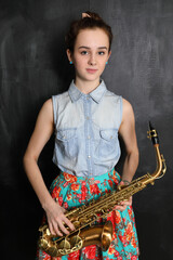 Portrait of young girl in floral skirt with saxophone in front of black wall