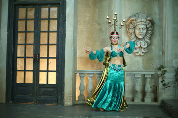 Beautiful woman in green dress decorated with pearls and chandelier on her head performs Arabic dance
