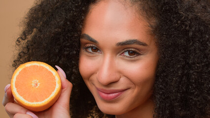 Smiling ethnic model girl African American woman hold half healthy orange fruit shake head with curly hair curls haircare shampoo balm with citrus beauty skin care organic cosmetics studio background