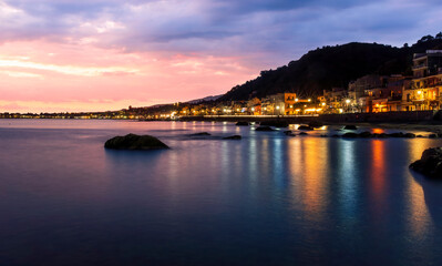 Fototapeta premium evening or night landscape of evening town coastline in golden lights and sea gulf with calm water and nice reflections with beautisul sunset sky on background