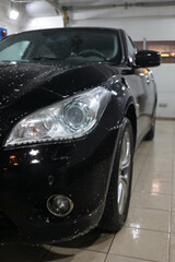 Naklejka premium Front of black car with detergent drops during washing
