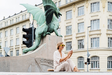 Young woman using smart phone sitting on Dragon bridge in Ljubljana. Travel Explore Slovenia, Europe - 762270162