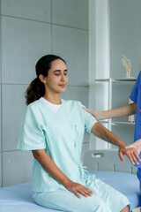 Patient in hospital attire closes eyes while therapist gently supports neck, indicating trust during examination. Individual in clinical garb relaxes under physiotherapist's care,