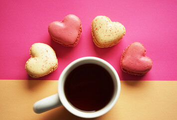 Heart-shaped macarons next to a cup of tea on a pink and yellow background