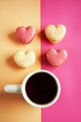 Heart-shaped macarons next to a cup of tea on a pink and yellow background