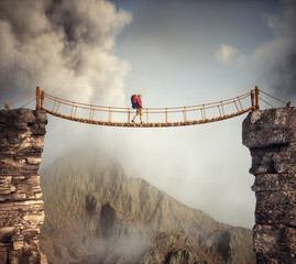 Hiker walking on a suspension bridge between mountains. - 762272335