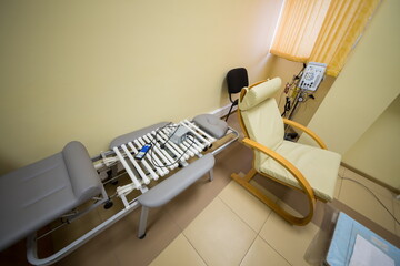 Grey bed for massage with white rolls and arm - chair at the rehabilitation center.