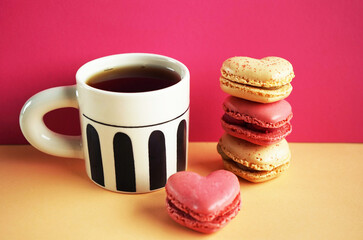 Heart-shaped macarons next to a cup of tea on a pink and yellow background