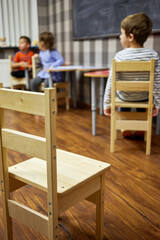 Three children in children club classroom, focus on chair.