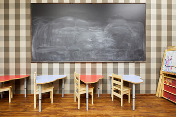 Blackboard on wall and desks with chairs in classroom at chidren club.