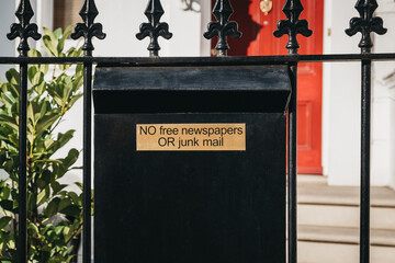 Close up of a black post box with "no free newspapers or junk mail" sign on a fence.