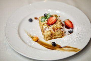 Layer cake with mint, strawberry, blueberry and sauce on plate.