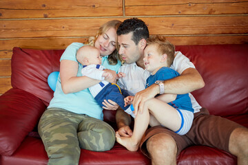 Family of fours sits on red leather sofa in room with wooden panelled walls.