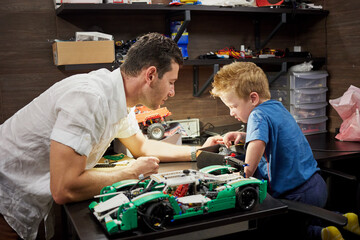 Father and little son build cars models on table in garage.