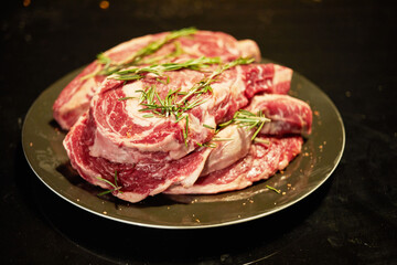 Pile of raw rib-eyes with rosemary and pepper on plate.