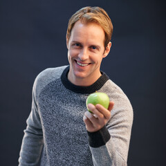 Man, apple and smile in studio portrait with choice for detox, diet or health by dark background....