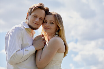Young smiling bearded man and woman stand with their heads pressed together against cloudy sky.