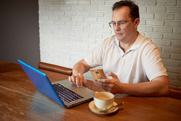 Man sits at table with laptop, smartphone and cup of coffee.