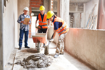 Senior male contractor supervising masons mixing mortar at corridor in incomplete house