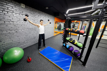Man works with dumbbells in room of fitness studio.