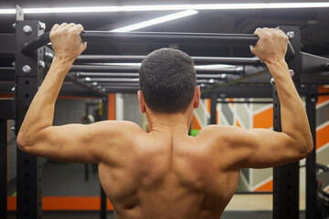 Naklejka premium Man chins up in fitness hall, rear view.