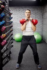Man doing exercises with two red kettlebells in gym hall.