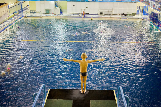 Little boy stands on diving-tower in Universal sports and entertainment complex. Pool includes swimming pool, children bath and jumping bath.