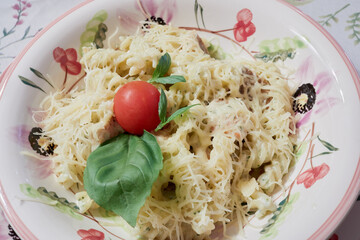 Pasta with chicken breast, tomato and leaves of basil on plate.