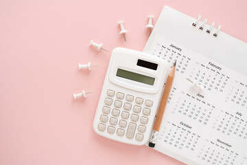 calculator, pencil on calendar with thumbtack on pink background including copy space
