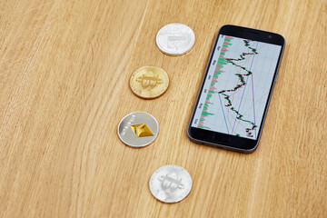 Smartphone with financial chart, bitcoin, litecoin, ethereum on wooden desk.