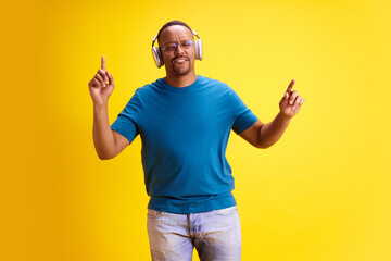 Cheerful African-American man in casual clothes listening to music in headphones and dancing...