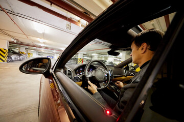 Man sits on driver seat in modern car at underground parking.