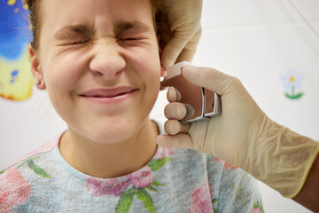 Doctor hands doing ear piercing to teenage girl.