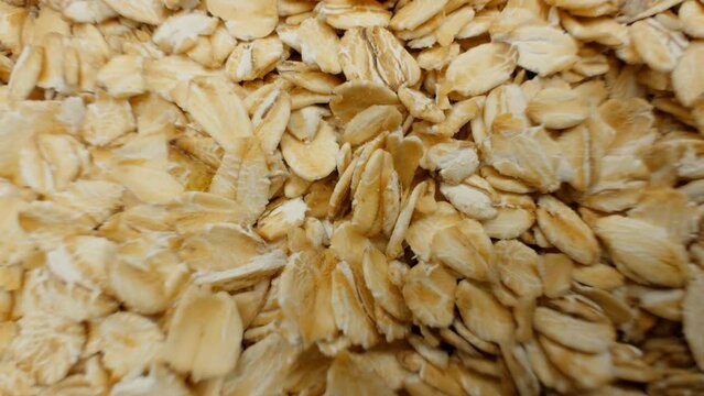 Uncooked oatmeal flakes texture close up. Rotation. Pile of uncooked rolled oats rotating. Oatmeal. Oat flakes. Dry oat flakes grains background. Food background. Gastronomy concept, organic food.