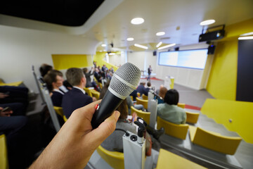 Closeup male hand holding microphone in auditorium, shallow dof.
