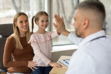 Happy family mother and daughter at appointment with male doctor, healthy girl giving man pediatrician high five, clinic interior - Powered by Adobe