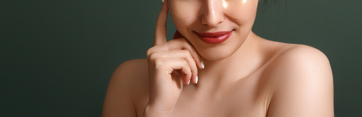 Young woman keeps eyes closed lips rounded touches face gently applies collagen patches undergoes...