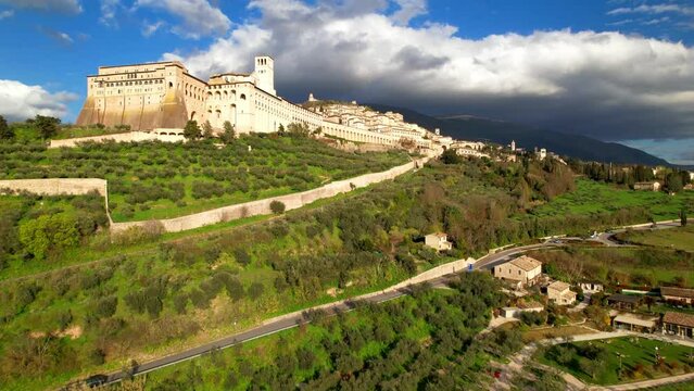 Italy Assisi aerial flight to medieval Basilica of Saint Francis cinematic dramatic clouds light over town scenery 4k drone landscape travel destination