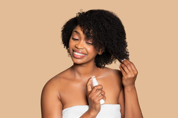 Happy black woman applying hair product on neutral backdrop