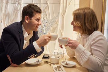 Smiling man and woman sit at table in cafe talking and drinking coffee.