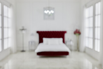 Interior of spacious white bedroom with large red bed, chandelier, flowers, windows on both sides,...