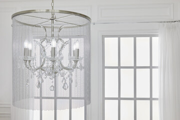 Six-bulb chandelier with beads pendants on ceiling in white room against latticed window.