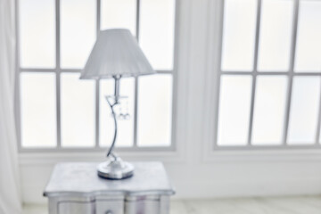 Table-lamp on bedside table against latticed window in room, image out of focus.