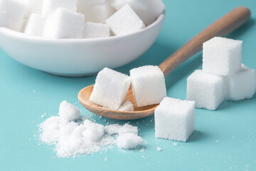 Sugar cube on wood spoon, closeup on blue background