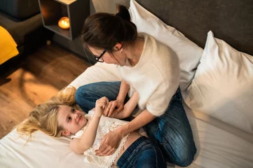 Poster Mother and child girl in bedroom cuddling on cozy warm comfortable bed in hotel room © zinkevych