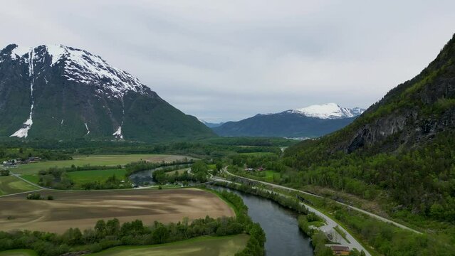 Dramatic, snowy mountain Setnesfjellet, Rauma River, and trees in Romsdalen Valley, Rauma, Norway
