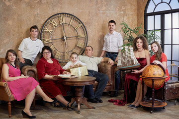 Family of eight members in room decorated in vintage style with large clock, mock ship, globe, old sofa.