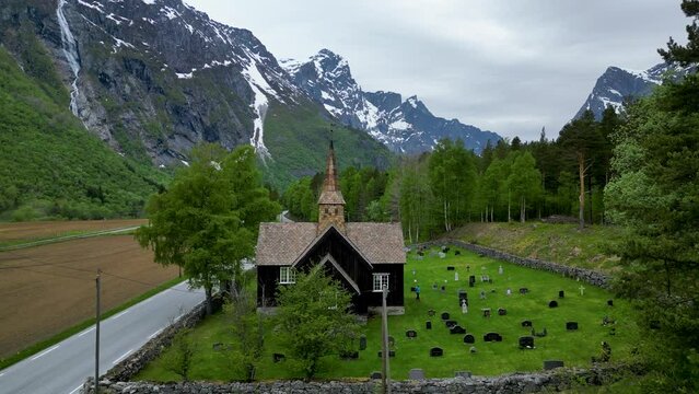 Brown, wooden Kors Kirke church and cemetery in Romsdalen valley, Rauma, Norway. Trollwall behind.